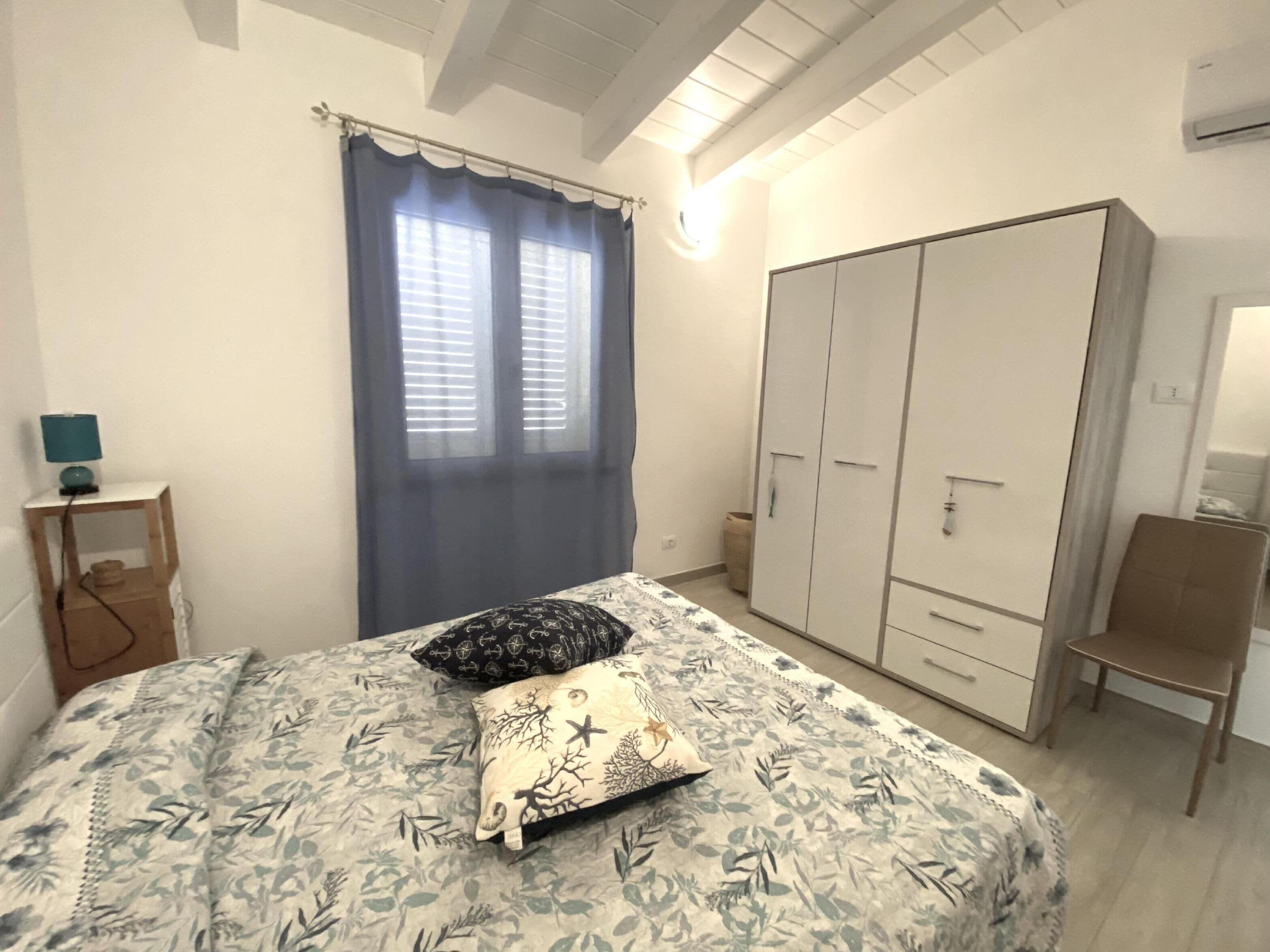 Une chambre à coucher comprenant un lit, une armoire, une table de chevet avec une lampe et une fenêtre avec des rideaux.