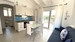 A modern kitchen with white cabinets, a dining table with chairs, and a view to the outside. - Residence La Marina (Isola Rossa)