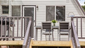 A wooden deck with a railing, a small table with a vase, and a sign that reads 'AT THE BEACH'. - Beach Chalet - Unique Triangular Beach House (Mollymook Beach)