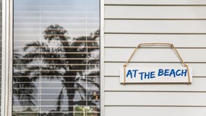 A window with horizontal blinds and a sign on the wall that reads 'AT THE BEACH'. - Beach Chalet - Unique Triangular Beach House (Mollymook Beach)