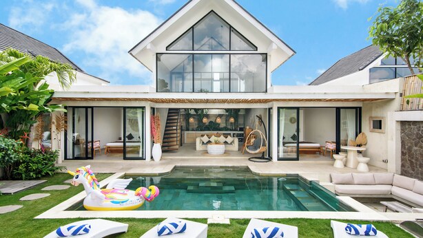 Una casa moderna con piscina, sillas de descanso y un flotador con forma de unicornio.