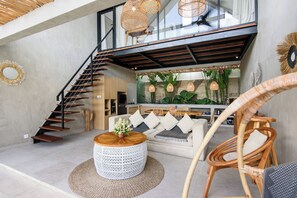 A spacious living area with a staircase, a round coffee table, a sofa with cushions, and wicker furniture. - La Joie Villa by Tasvan (Badung)