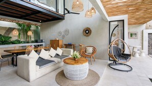 Una sala de estar moderna con sofá, mesa de centro redonda, sillón de mimbre y lámparas colgantes de mimbre.
