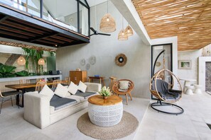 A modern living room with a sofa, round coffee table, wicker chair, and hanging wicker lamps. - La Joie Villa by Tasvan (Badung)