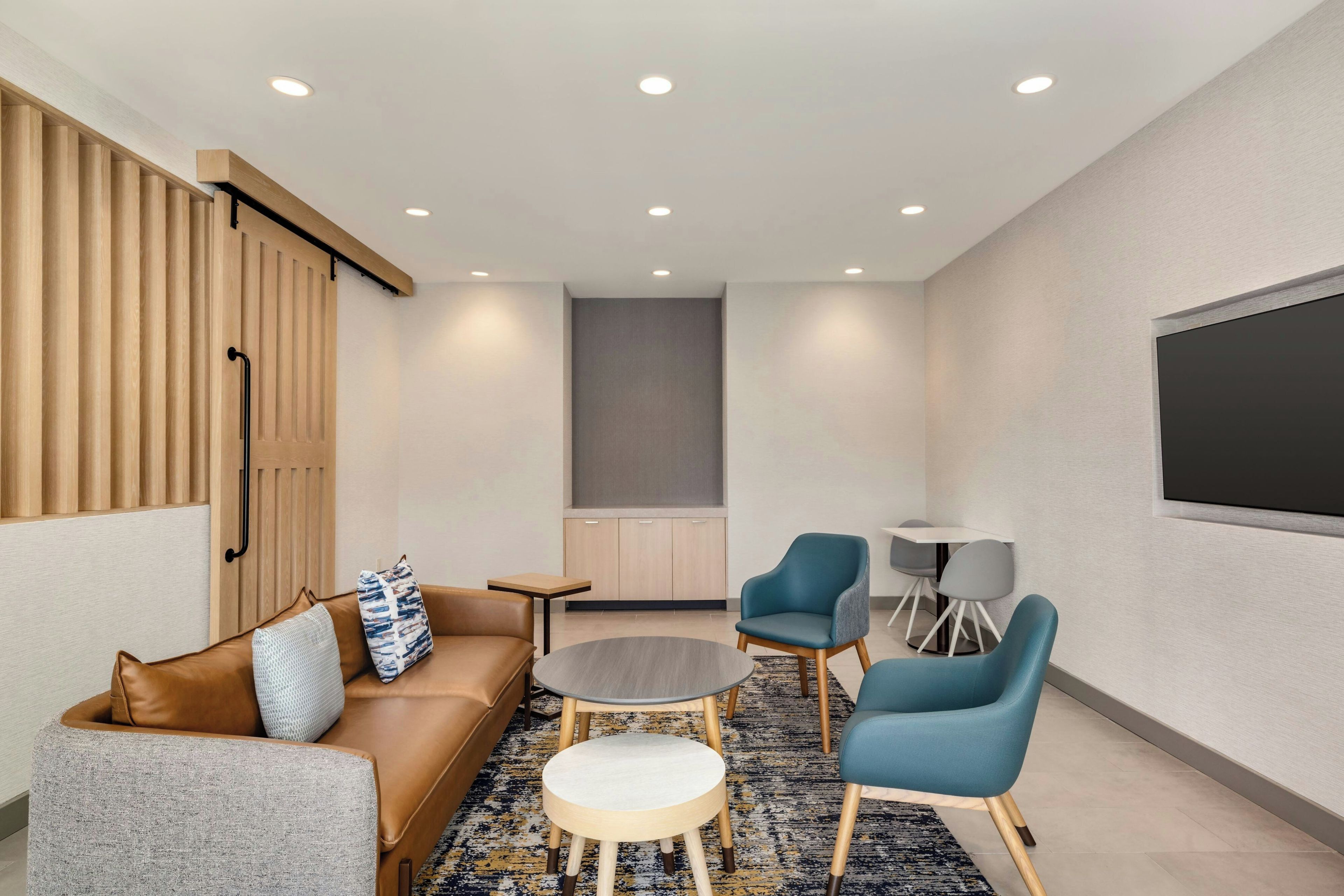 Una sala de estar moderna con un sofá, dos sillones, una mesita de centro y un televisor montado en la pared.