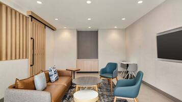 Una sala de estar moderna con un sofá, dos sillones, una mesita de centro y un televisor montado en la pared.