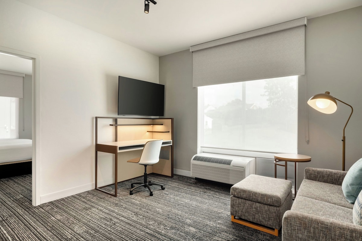 Habitación de hotel con cama, escritorio y silla, televisor, ventana con vistas y lámpara.