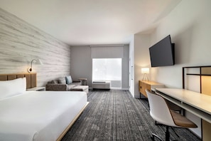 Habitación de hotel con una cama grande, un escritorio con silla, un televisor montado en la pared y una ventana con vistas.