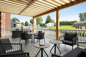 Un patio cubierto con mobiliario exterior, una parrilla y vistas del barrio.