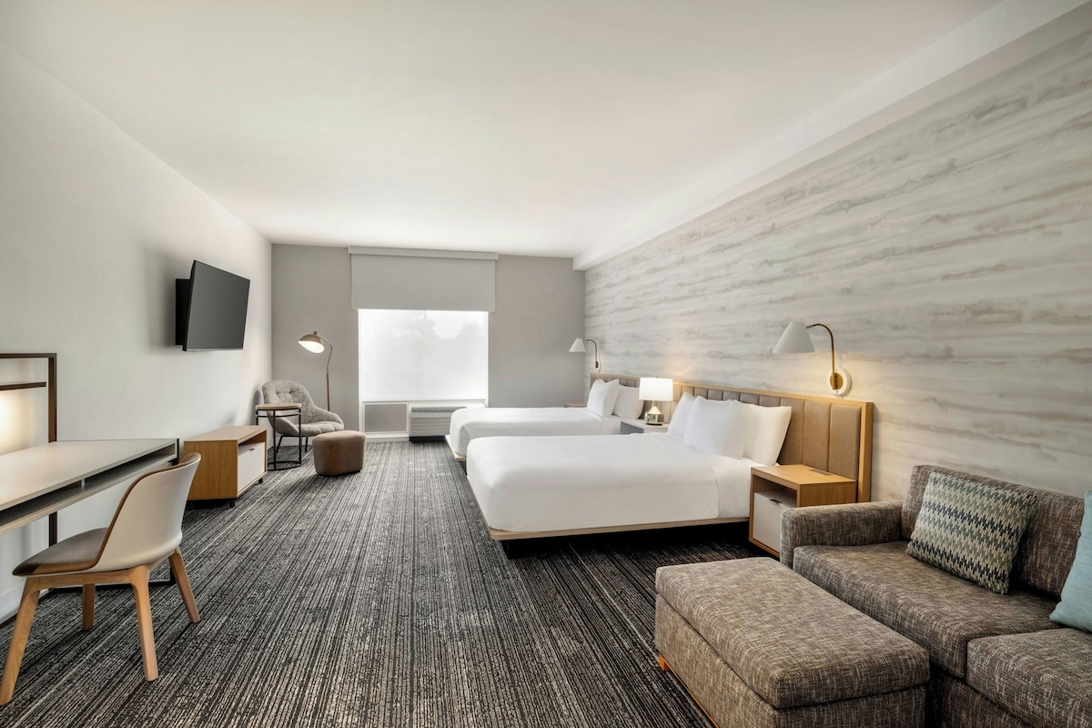 Una habitación de hotel con una cama, dos mesitas de noche, un escritorio, una silla, un sofá y un televisor.