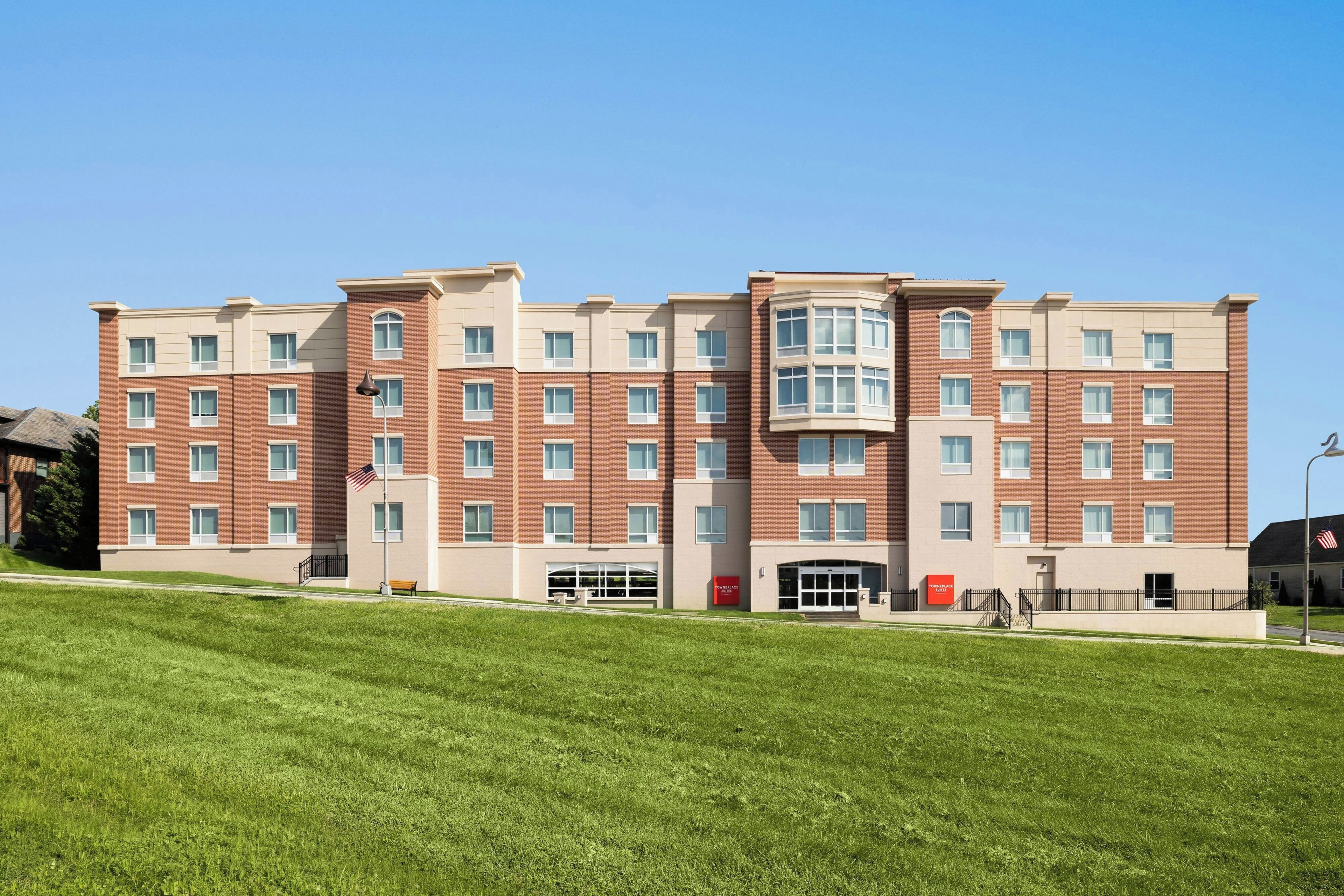 A multi-story hotel with a central entrance, a flagpole with an American flag, and a well-maintained lawn in the foreground.