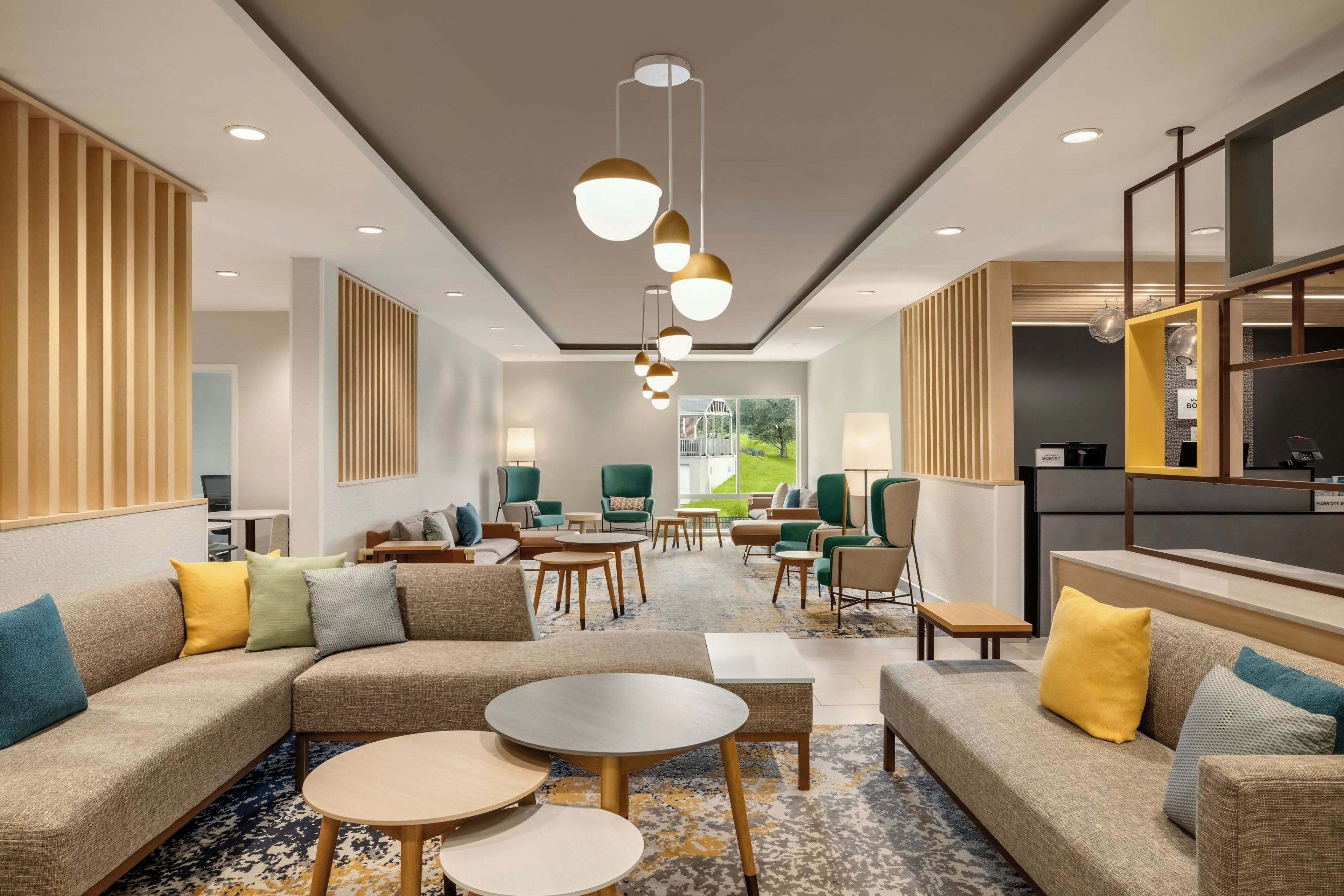 A hotel lobby with a sectional sofa, round tables, and a large window offering a view of the outdoors.