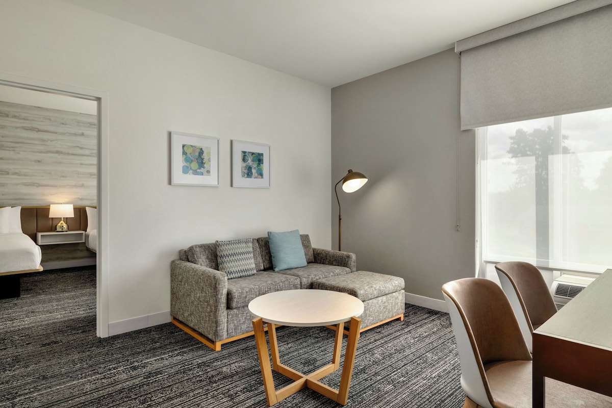 Habitación de hotel con cama, sofá, una mesita y una silla. Dos cuadros enmarcados decoran la pared.