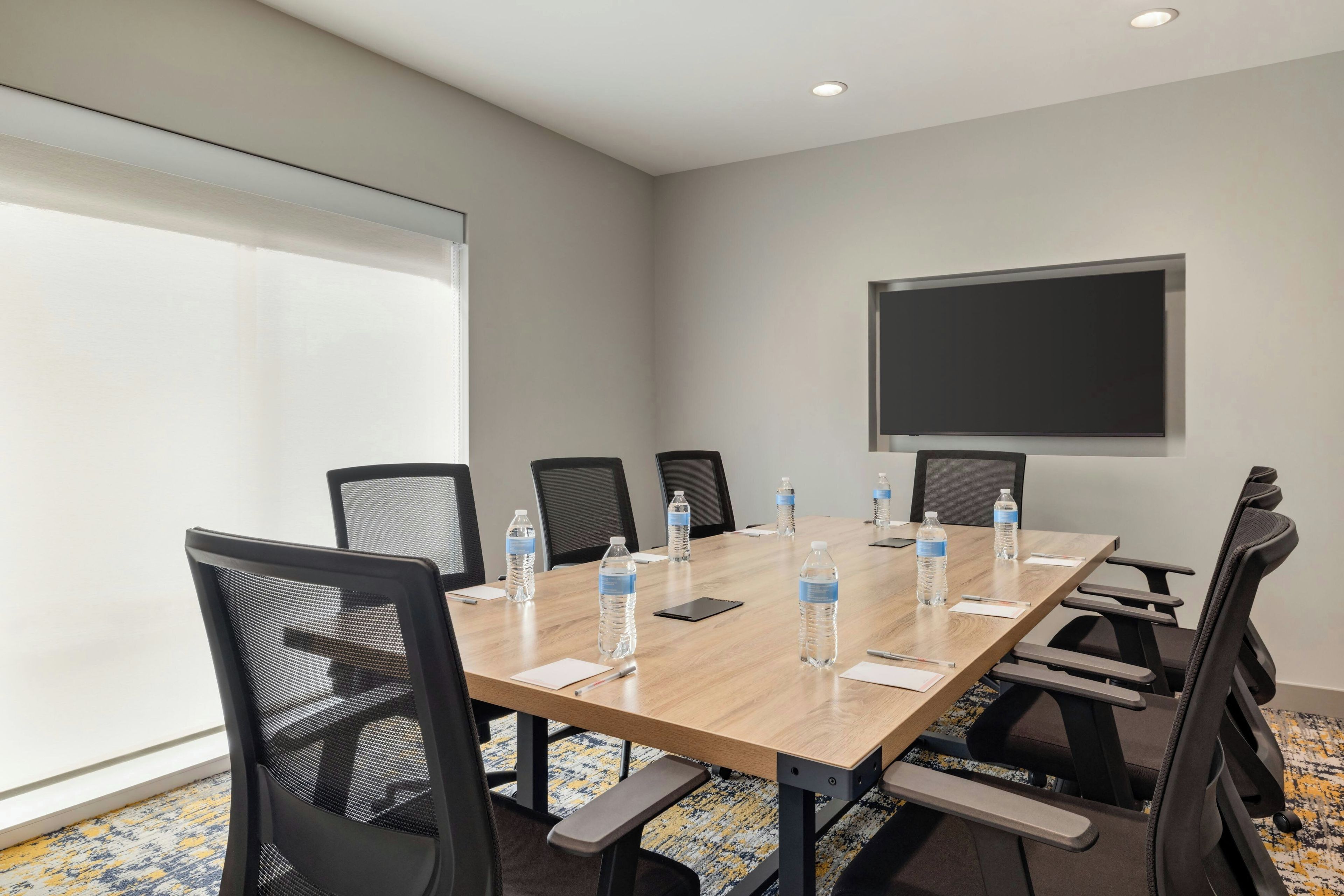 A conference room with a long table, chairs, water bottles, and a projector screen.