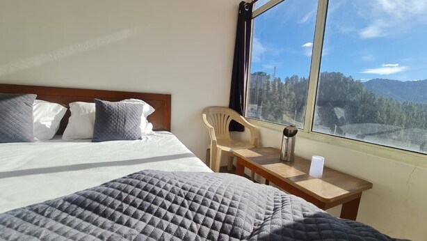 Habitación de hotel con cama, mesa, silla y ventana con vista a la montaña.