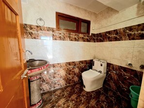 Un baño con piso de mármol, un inodoro, un lavabo y un balde verde.