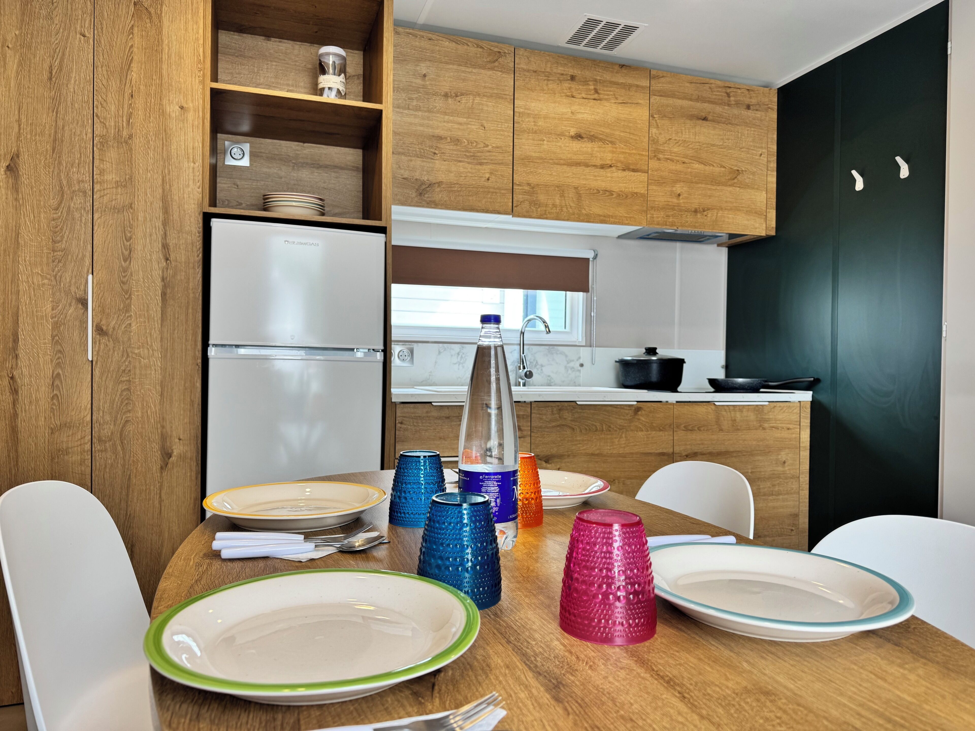 A compact kitchen with wooden cabinets, a white refrigerator, a sink, and a dining table set with plates and cups.