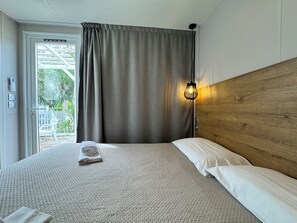 A hotel room with a bed, a wooden headboard, a hanging light fixture, and a view through a door.