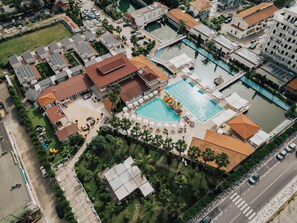 Vista aérea de un complejo turístico con múltiples piscinas, tumbonas y un tobogán de agua central.