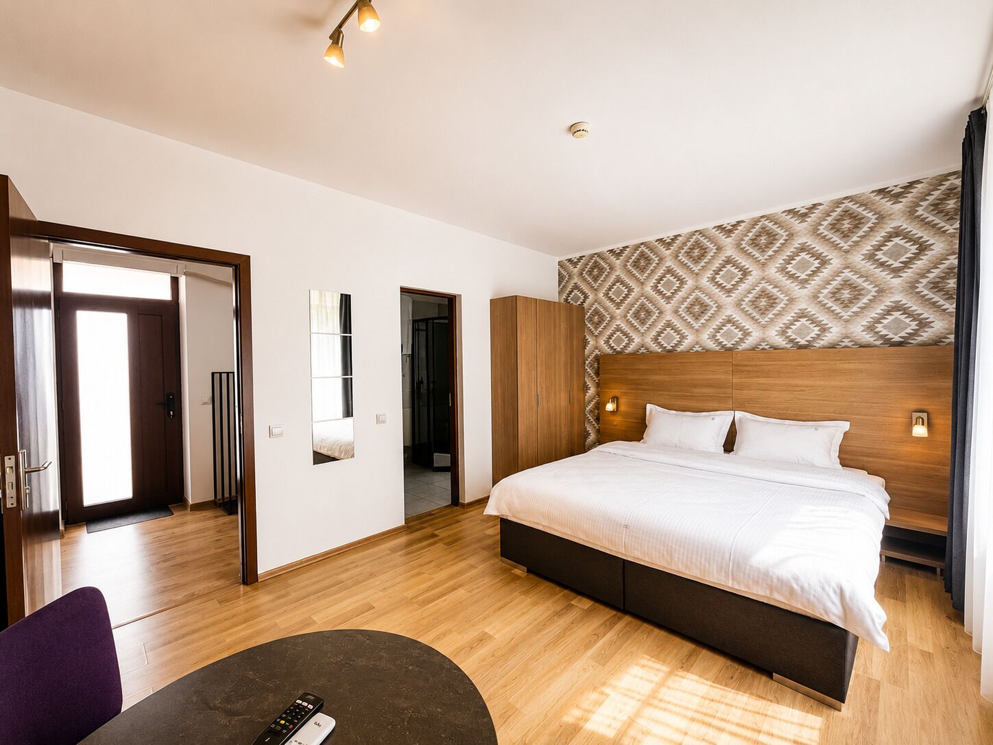 Une chambre d’hôtel moderne avec un grand lit, une tête de lit en bois, une petite table et un miroir.