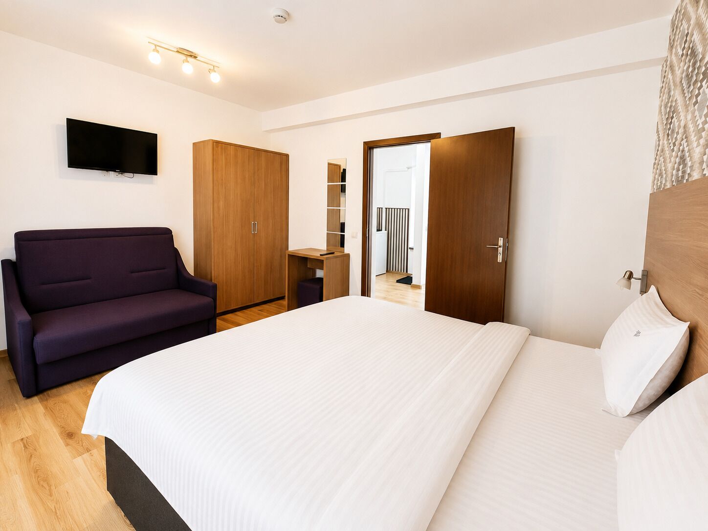 A modern bedroom with a bed, a sofa, a wardrobe, and a television.