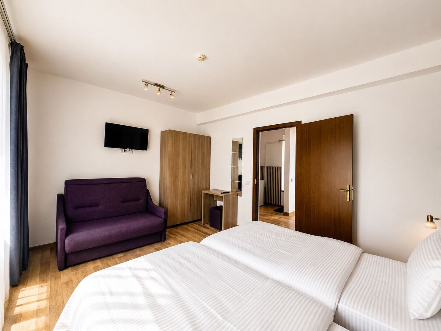A hotel room with a bed, a sofa, a TV, a wardrobe, and a mirror.