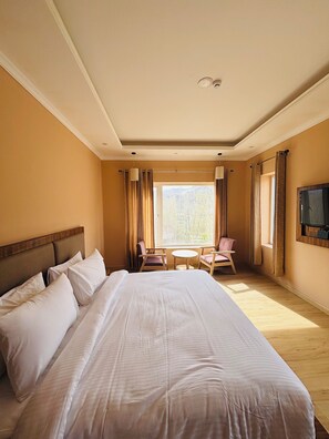 A hotel room with a large bed, a small table with chairs, a TV mounted on the wall, and a window with curtains. - Hotel Dekiling by Eastlynn Collections (Leh)