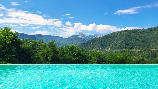 A swimming pool with clear blue water, surrounded by lush greenery and mountains in the background.