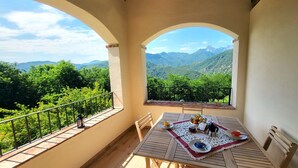 A balcony with a table set for two, overlooking a mountainous landscape.