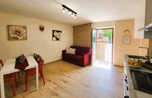 A living room with a red sofa, a white table with chairs, a kitchen area with a sink and stove, and a door leading outside. -  NEW! Perfect for 2! Private Pool, mountain Views, covered terrace. Romance! (Toscana)