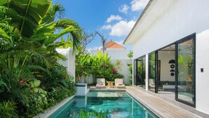 A modern pool area with a clear pool, surrounded by lush tropical plants and a white building with large windows. - Infinity Villa by Tasvan (Badung)