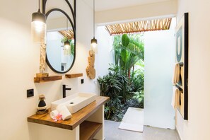 A modern bathroom with a wooden vanity, a large mirror, and a view of a tropical garden. - Infinity Villa by Tasvan (Badung)