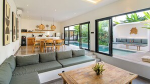 A modern living area with a sofa, dining table, and a view of a swimming pool. - Infinity Villa by Tasvan (Badung)