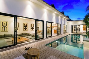 Una casa moderna con piscina, terraza de madera y sala de estar con sofá y mesa de centro.