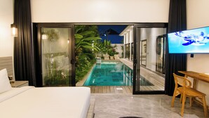A bedroom with a bed, a TV, a wooden desk, and a glass door leading to a pool area. - Infinity Villa by Tasvan (Badung)