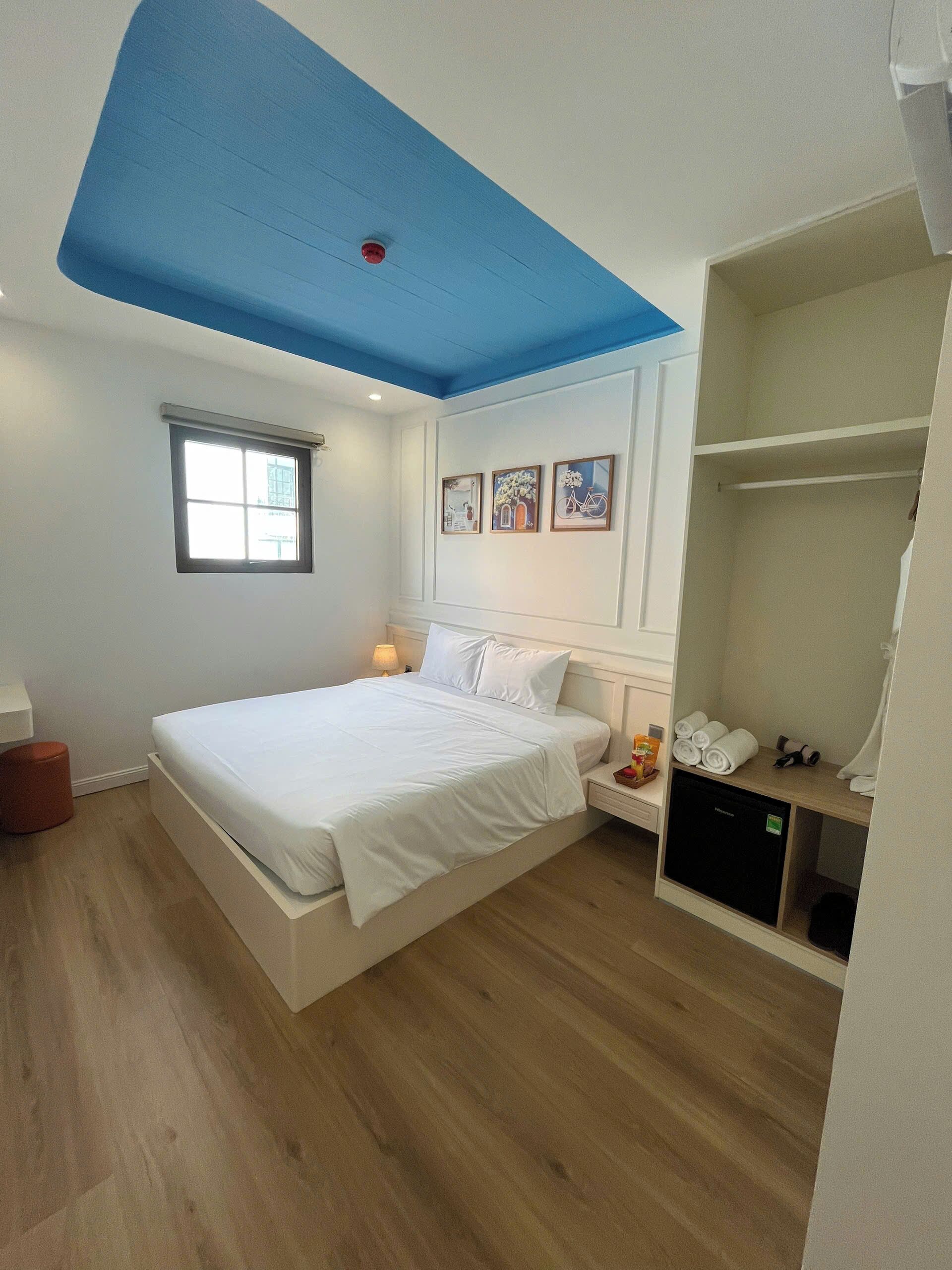 A bedroom with a bed, a window, a bedside table with a lamp, a wardrobe, and a ceiling light fixture.