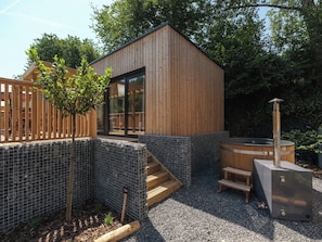 A wooden cabin with a glass door, a hot tub, and a wooden deck.