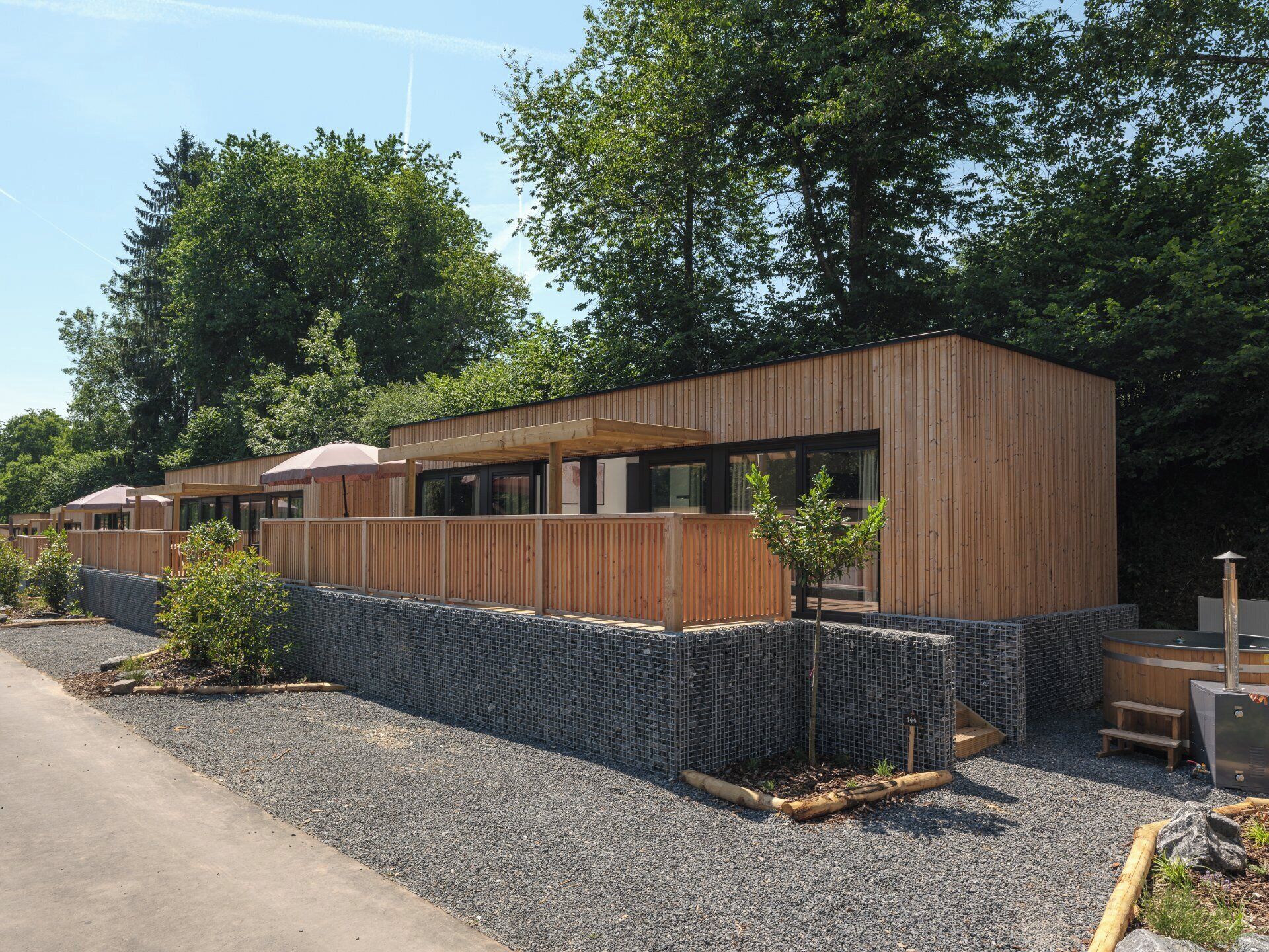 A modern building with a wooden exterior, a covered outdoor seating area, and a small garden area with plants and a wooden bench.
