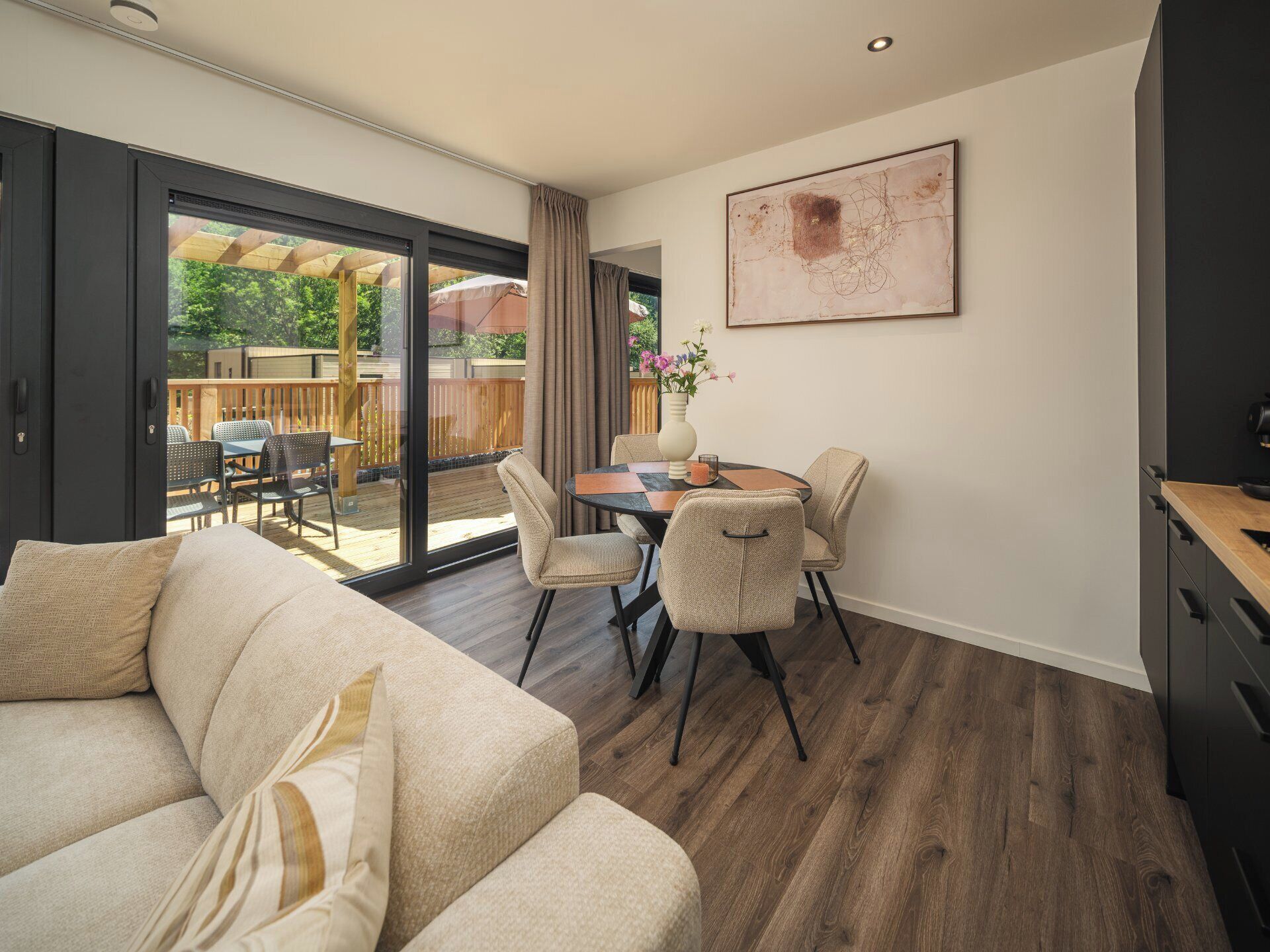 Een moderne woonkamer met een bank, een eettafel met stoelen, een keukenhoek en een glazen schuindeur naar een terras.