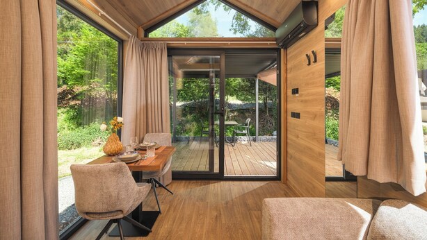 A modern interior with a dining area, wooden flooring, and large windows offering a view of a garden.