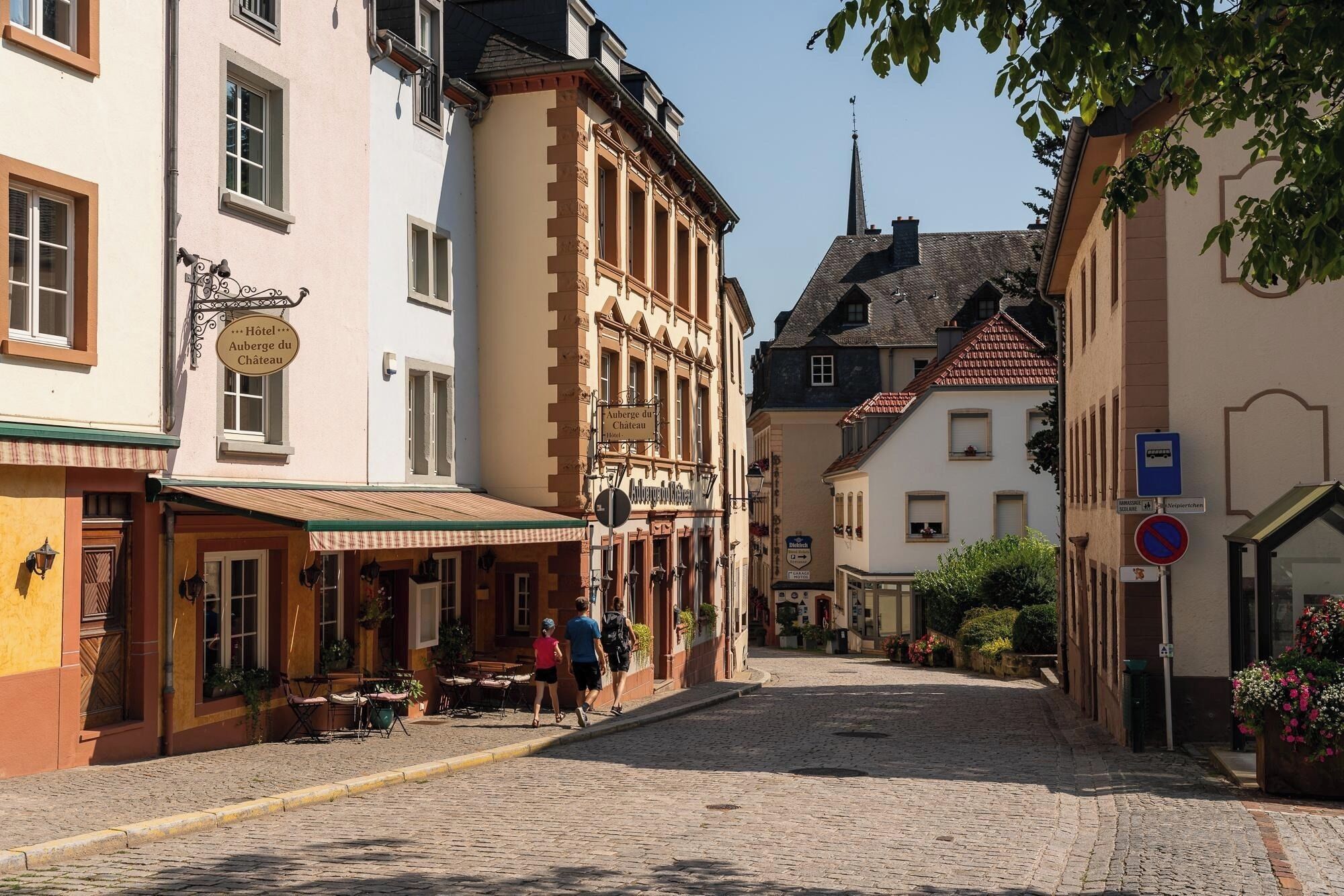 Une rue pavée bordée de bâtiments historiques, dont un hôtel doté d’une terrasse et d’un panneau indiquant la présence d’un restaurant à proximité.