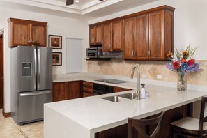 A modern kitchen with wooden cabinets, stainless steel appliances, a marble countertop, and a vase of flowers. - Ground floor Condo Steps from the Sand with Pool and Sunset Views (Playa Langosta)