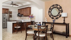 A modern kitchen with wooden cabinets, a central island, and a dining area with a glass table and chairs. - Ground floor Condo Steps from the Sand with Pool and Sunset Views (Playa Langosta)
