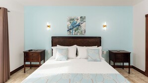 A bedroom with a large bed, two nightstands, a headboard with a painting, and wall sconces. - Ground floor Condo Steps from the Sand with Pool and Sunset Views (Playa Langosta)