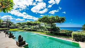 A clear blue pool with a view of the ocean, surrounded by well-maintained landscaping and a clear sky. - Ground floor Condo Steps from the Sand with Pool and Sunset Views (Playa Langosta)