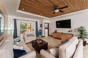 Ein modernes Wohnzimmer mit Deckenventilator, Flachbildfernseher und einer großen Topfpflanze.