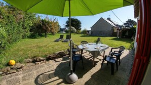 Een buitenterras met een ronde tafel en stoelen, een groene parasol en een stenen pad.