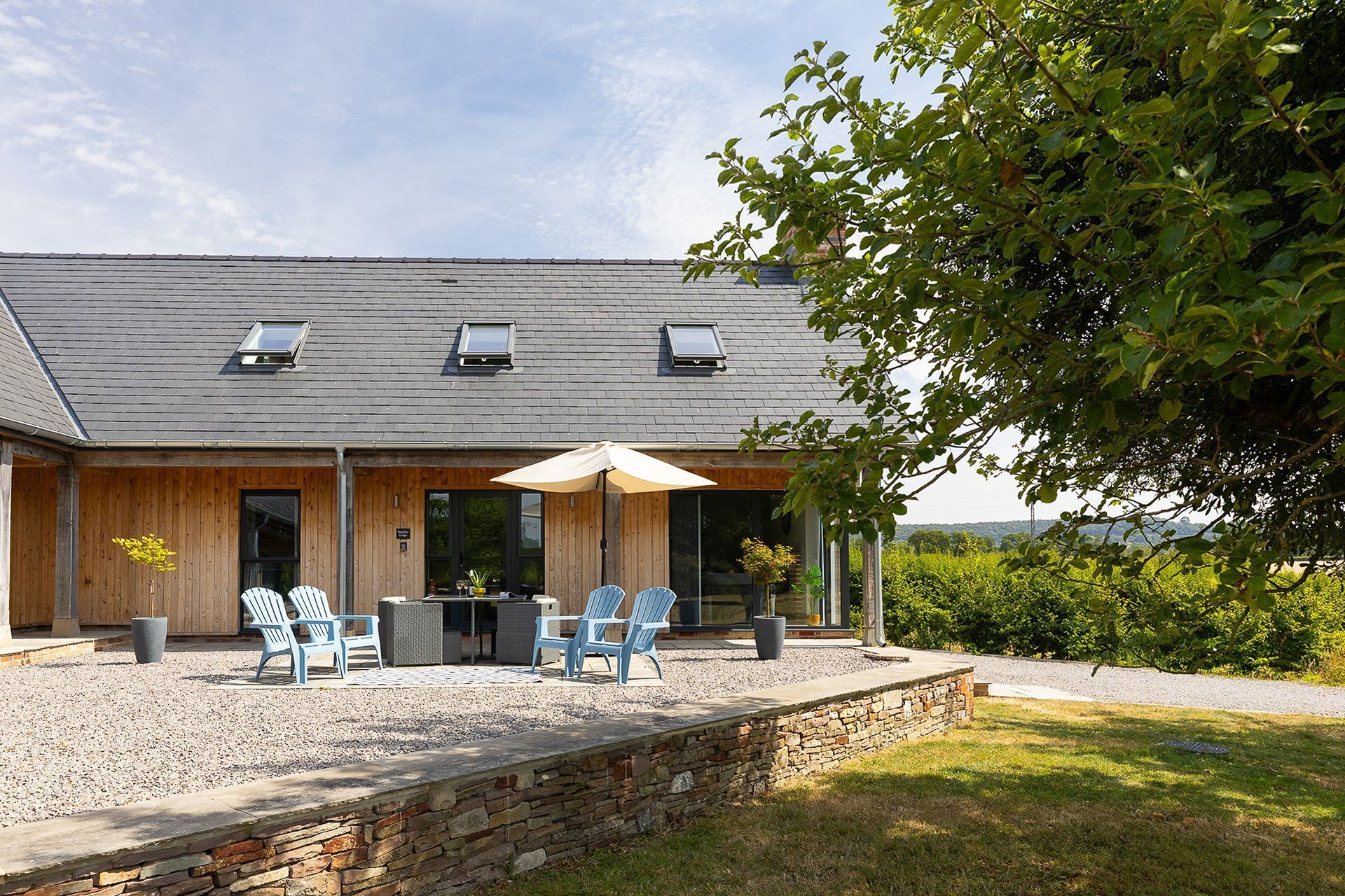 Ein Haus mit überdachter Terrasse, Gartenmöbeln und einer Steinmauer.