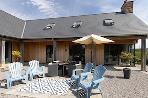 Ein überdachter Patio-Bereich mit Gartenmöbeln und einem Tisch, ein Holzbauten mit geneigtem Dach und Dachfenstern.