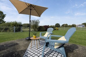 Een terras met twee stoelen, een tafel, een grote parasol en een potplant.